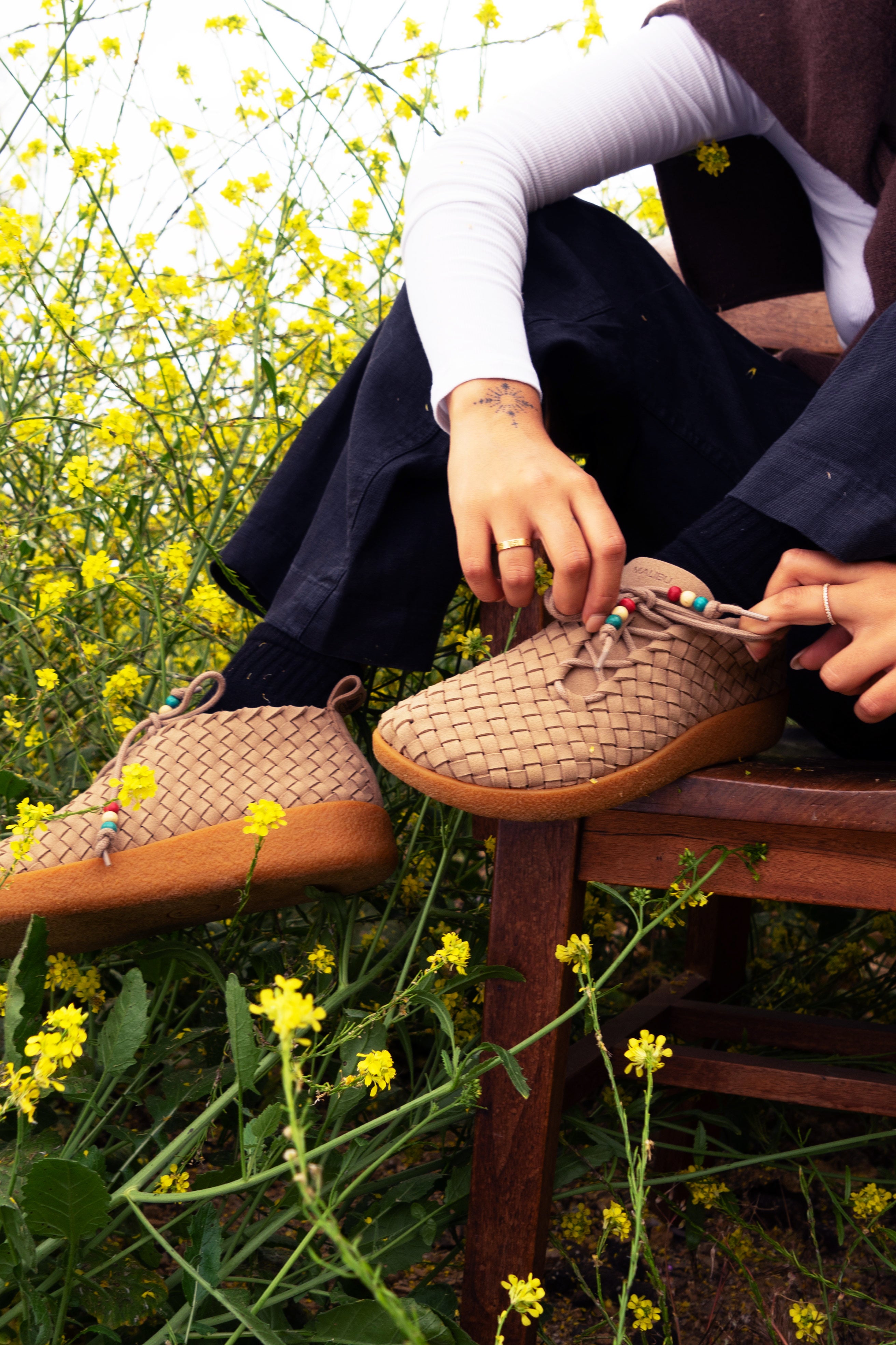 Lifestyle photo of women tying the laces of Malibu Sandals beige matador chukka sandal on a chair with a background of flowers wearing black socks, black pants and white long sleeve top