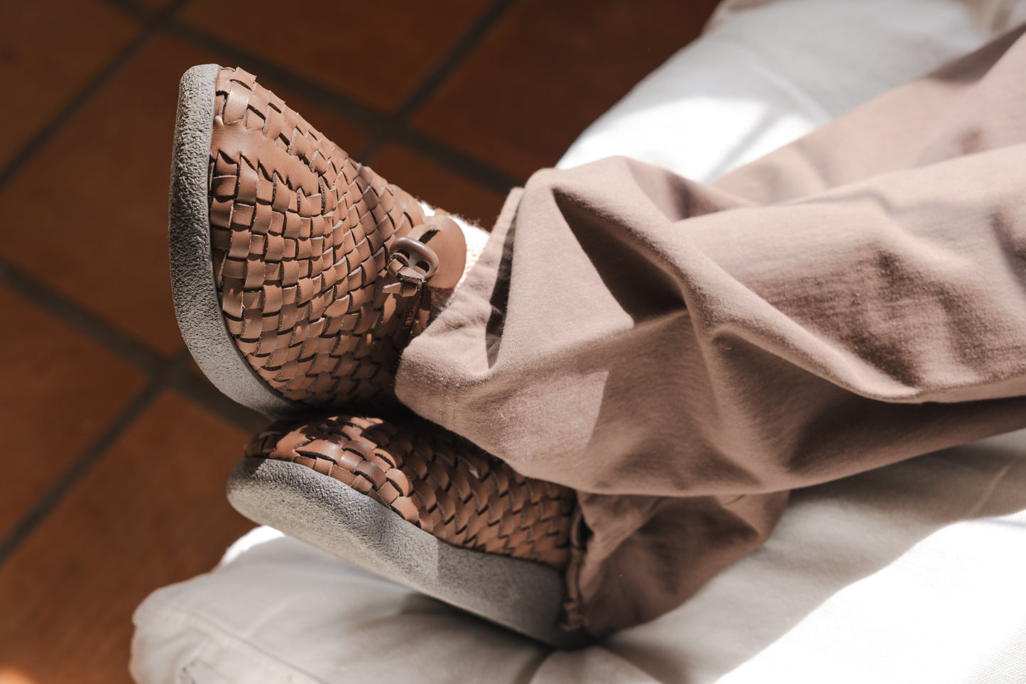 Close up photo of the malibu sandals Latigo vegan lather in Bison color way being worn with born pants and resting on the edge of a white couch.