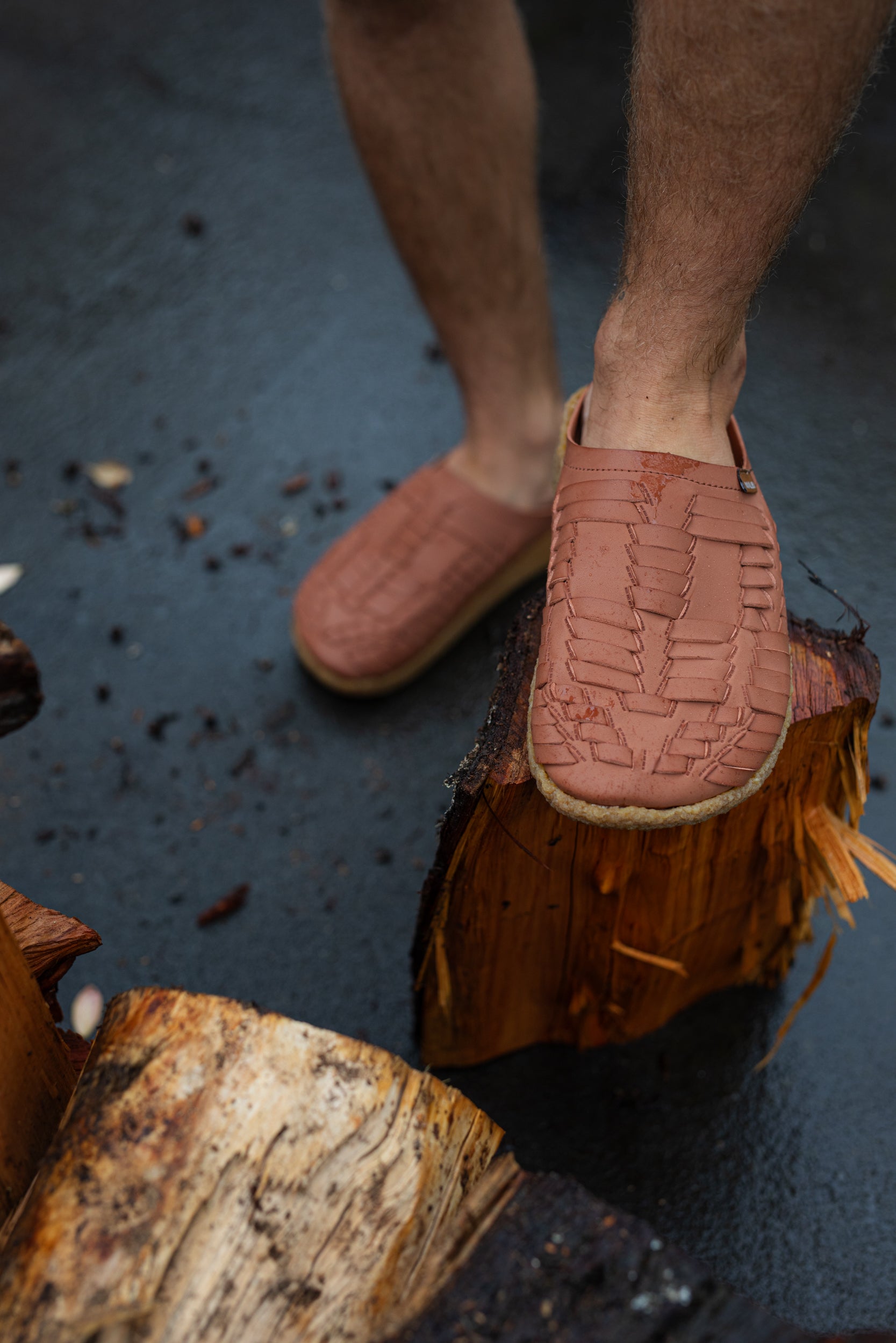 close up photo of malibu sandals thunderbird clog stepping on a log with a wet ground background