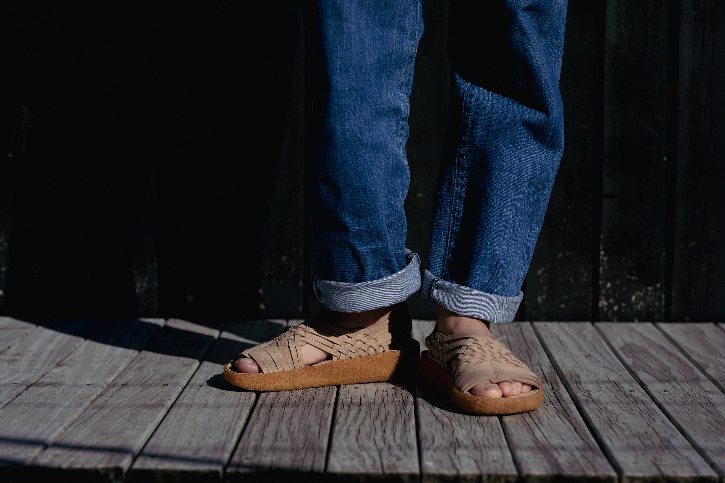 lifestyle photo of Malibu sandals canyon in beige color and crepe sole being worn with cuffed blue denim jeans and wood flooring